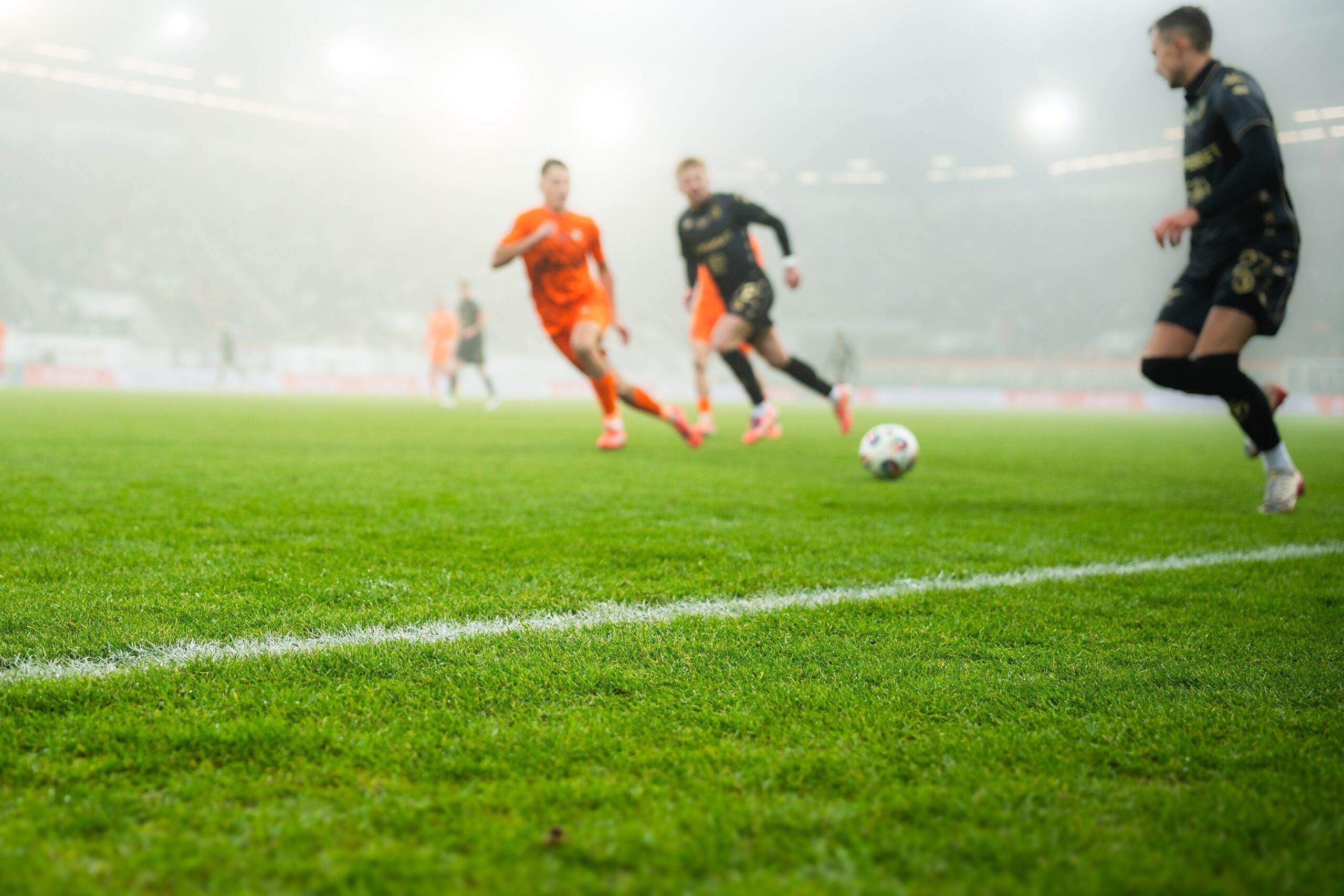 grass and sideline on the football pitch at the stadium and player's legs at the background
